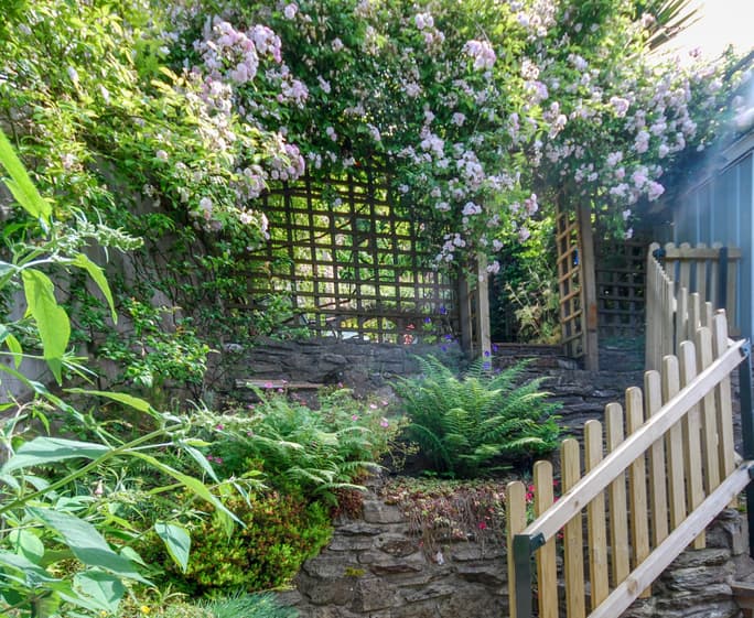 French doors open on to the rear decked terrace and patio area, steep steps lead up into the raised and layered gardens
