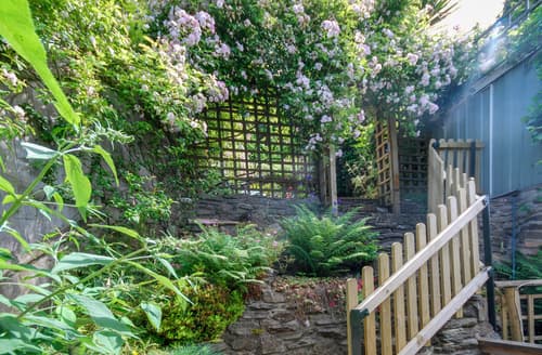 French doors open on to the rear decked terrace and patio area, steep steps lead up into the raised and layered gardens