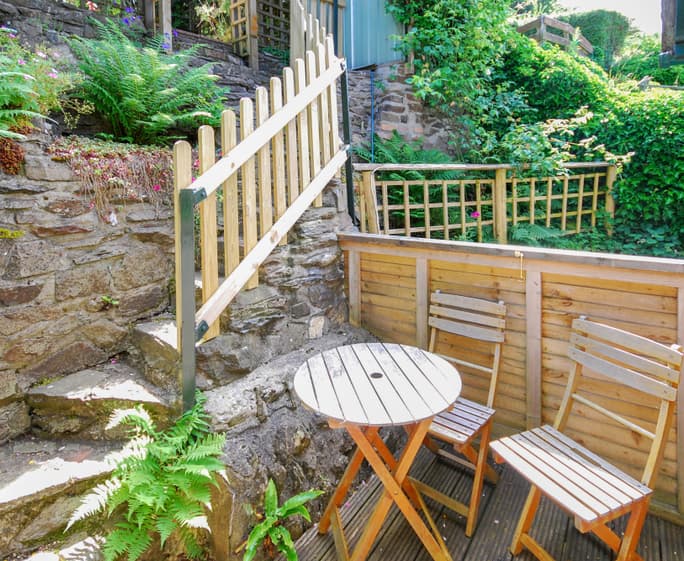 French doors open on to the rear decked terrace and patio area, steep steps lead up into the raised and layered gardens