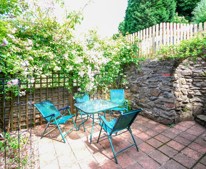 French doors open on to the rear decked terrace and patio area, steep steps lead up into the raised and layered gardens